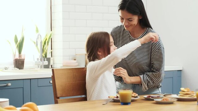 Young happy woman having a breakfast indoors at home with her daughter and hugging
