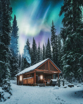 Aurora borealis over wooden cottage with smoke on snow in pine forest at Yoho national park