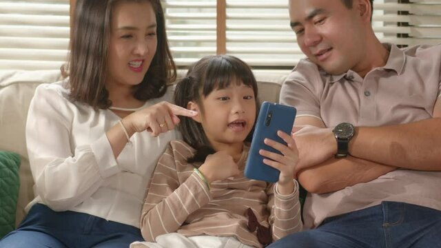 Happy  Smiling Asian Family are Relax sitting on a couch using a smart phone and having a video call chatting or taking a selfie with a mobile together fun and enjoying online communication at home