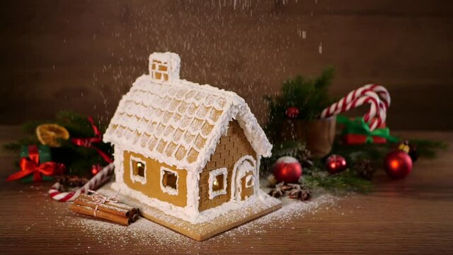 Sprinkling sugar powder (imitating snow) over gingerbread house on wooden table. Christmas atmosphere