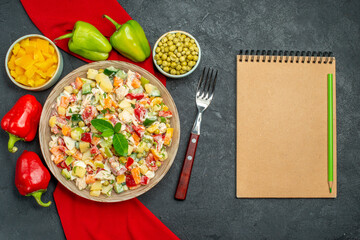 top close view of veggie salad on red napkin with veggies notepad and fork on side on dark grey background