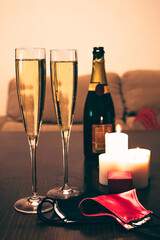 Close-up of two glasses of champagne on a table in a living room with two face masks.
