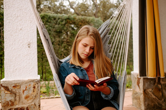 chica joven pensativa leyendo un libro en el jardín trasero de su casa