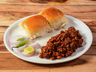 Mutton Kheema pav or keema Pav is a spicy curry dish made up of minced mutton cooked with onion, tomatoes, served with buns or pav, isolated over a rustic wooden background, selective focus