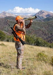 adult rifle hunter blowing elk calls through bugle tube in mountains