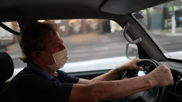 Older man looking at rear view mirror while driving and wearing covid-19 face mask