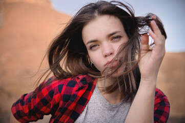 Portrait of an attractive Caucasian young woman in a checkered red shirt against a background of mountains. Bliss and pleasure in the mountains. The wind blows your hair