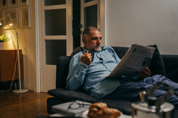Fototapeta premium man laying on sofa and reading newspapers at his home