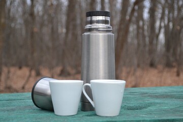 
Thermos and two cups on the table in nature.