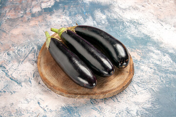 Top view of three natural fresh eggplants side by side on wooden tray on ice background