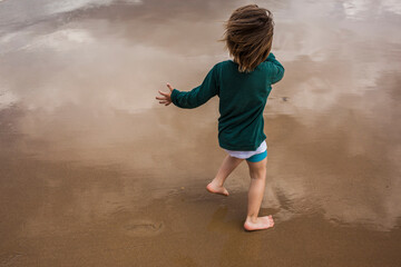 niño rubio de pelo largo y en pantalón corto jugando descalzo en la orilla de la  playa 
