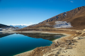 Fototapeta na wymiar A lake high in the mountains in winter with the blue sky and reflection in the water