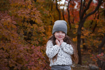 Cute kid girl 4-5 year old wearing sweater and jacket in park. Looking at camera. Autumn season. Childhood.