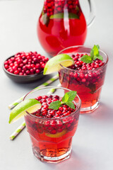 Lingonberry and lime punch or limeade in glass and pitcher on gray background, vertical