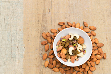 Fototapeta na wymiar A variety of nuts and bean are in a bowl on the wooden background at the right of the image, top view, flat lay, top-down.