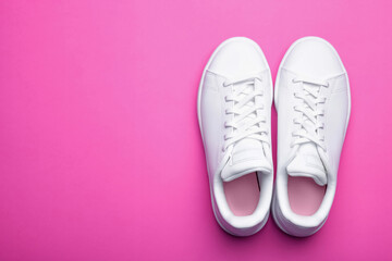 Fototapeta na wymiar Pair of stylish sport shoes on pink background. Top view of white sneakers on color background with space for text 