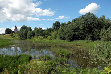 Fototapeta na wymiar Beautiful rural landscape with quiet pond, old church and clouds on the sky in bright summer day