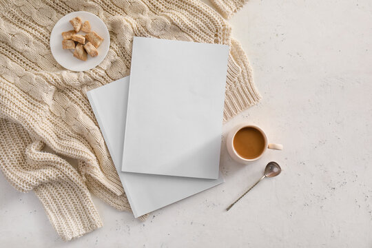Blank magazines, coffee, sweets and sweater on light background