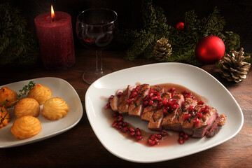 Roasted duck breast with pomegranate seeds and duchess potatoes for a festive holiday meal, red wine, candle and Christmas decoration on a dark wooden table, selected focus, narrow depth of field