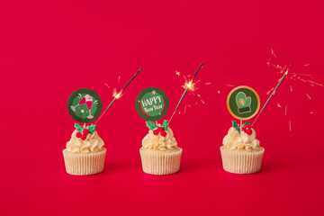 Tasty Christmas cupcakes with sparkler on color background