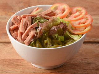 Salami with green leaf salad, Delicious fresh salad of salami and mixed lettuce leaves, baby spinach, arugula, chard. served over a rustic wooden background, selective focus