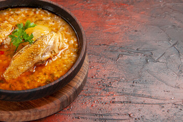 bottom close view chicken soup in wooden bowl on chopping board on dark red background with copy space