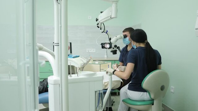 Medical Stomatology Concept. Doctor making teeth examination research survey using microscope in dentistry. Dentist is treating patient in modern dental office