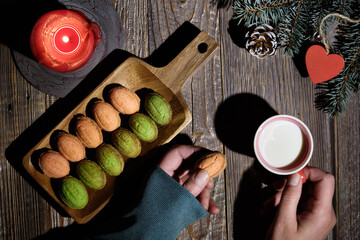 Walnut shape cookies with Dulce De Leche, sweetened condensed milk. Creative top view on dark wooden table with natural decorations. Cup of milk in hand. Fir twigs, hearts, candle, frosty pine cones.