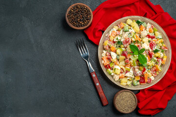 top close view of veggie salad on red napkin with fork and pepper on side and with free space for text on dark grey background