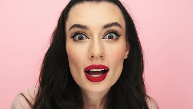 A surprised woman with red lips is peeping for something standing isolated over pink background in studio