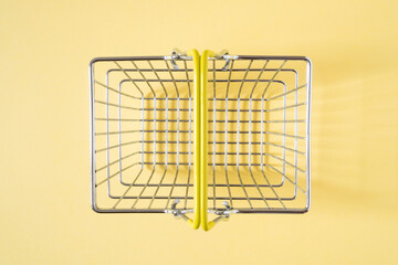 Empty shopping basket with yellow handle on beige background.Top view.