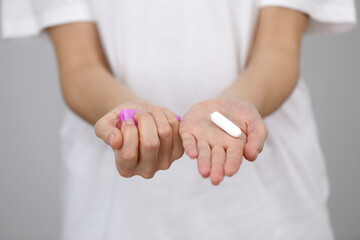 Close up view of young woman making choice between menstrual cup and tampon, on white background....
