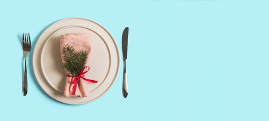 Banner with served table with empty plate and cutlery for celebration of Christmas and New Year. On plate is napkin with Christmas tree branch. Flatlay banner on light blue background. Top view.
