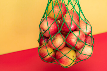 red apples in a green string bag on a yellow-red background