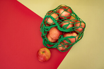 red apples in a green string bag on a red-green background in the top view