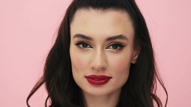 An attractive woman with red lips is eating bubblegum standing isolated over a pink background in the studio