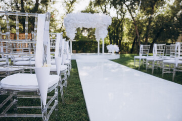 Wedding arch decorated with cloth and flowers outdoors. Beautiful wedding set up. Wedding ceremony on green lawn in the garden. Part of the festive decor, floral arrangement.