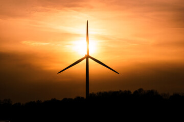 single wind turbine silhouettes at cloudy golden sunset