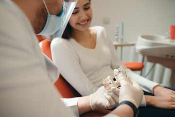 Dentist in a protective mask shows a Caucasian girl a model of the jaw