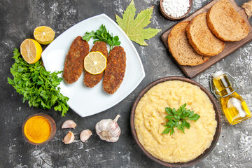 top view mashed potatoes cutlets on white plate bread slices on cutting board parsley lemon slices oil on dark background