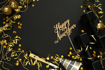 Black dumbbells, golden decorations, confetti, party hat and horn blower for New Year's Eve celebration. Healthy fitness lifestyle flat lay concept. Gym, workout New Year's resolution composition.