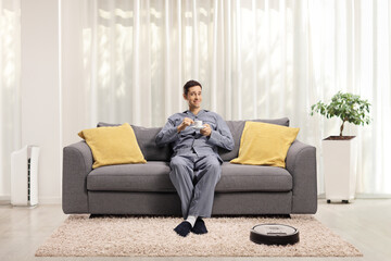 Robotic vacuum cleaner on the carpet and a man in pajamas sitting on a sofa