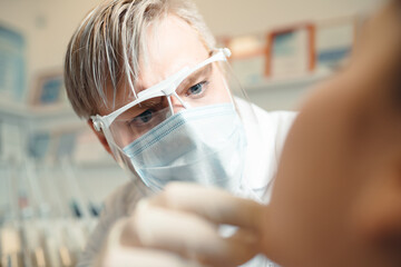 A dentist wearing safety glasses examines a client's teeth. Healthy teeth concept