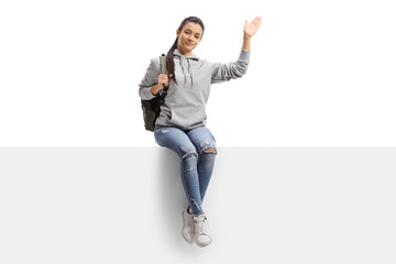 Cheerful female student sitting on a blank board and waving at camera