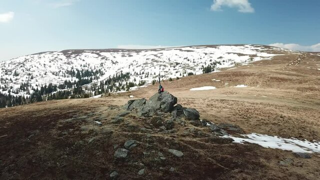 A drone capture of a couple with backpacks standing at the top of Seiner Kreuz, a peak in Austrian Alps. A wooden cross on the peak. Early spring in the mountains. Wanderlust. Achieving the goal
