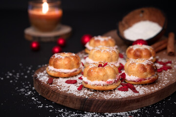 Goji berries, red shiny Christmas balls. Coconut shell full of flour, sprinkled over five small home baked cakes, filled with strawberry cream. Wooden board. Cinnamon sticks decoration. Burning candle