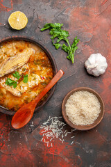 top view homemade chicken and rice soup in a bowl wooden spoon bowl with rice garlic parsley leaves on dark red background