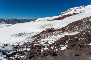 Rocks and white slopes of Elbrus, Caucasus. Snow-covered peaks and clear blue skies. Winter mountains, alpine skiing. Sunny snowy landscape. Panoramic mountain view.