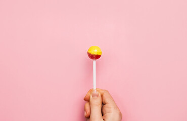 Colorful lollipop candy cane in hand. Strawberry banana sweetness on pink background. 