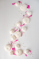 white meringues with pink petals in top view on white background